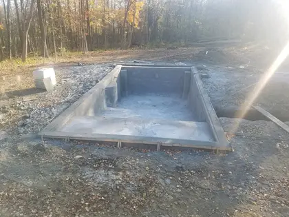 Freshly formed pool shell mid-construction on a wooded lot